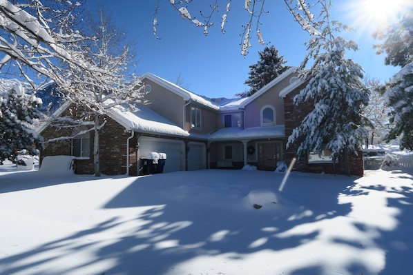 Una casa de dos pisos con un camino de entrada cubierto de nieve y un garaje.