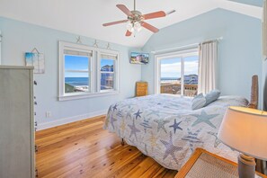 A bedroom with a bed, a ceiling fan, a view of the beach, and a window with curtains. - Semi-Oceanfront Dog Friendly Home w/ Private Pool, Hot Tub, Elevator, Game Room (Rodanthe)