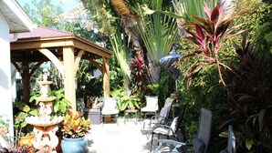 A covered patio area with a tiered fountain, outdoor seating, and various potted plants.