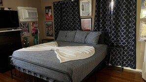 A bedroom with a bed, a dresser, a television, and posters on the wall.