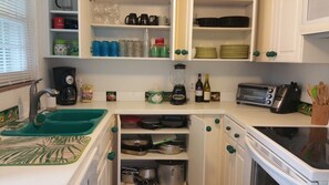 A kitchen with white cabinets, a sink, a coffee maker, a blender, a toaster, and various kitchen utensils.