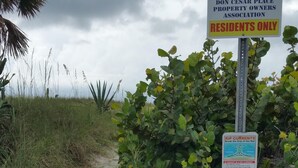 A private property entrance with a warning sign about rip currents and a no lifeguard notice.