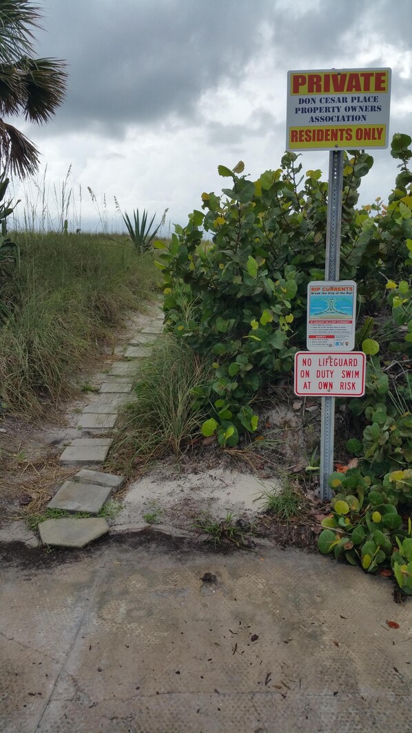 A private property entrance with a warning sign about rip currents and a no lifeguard notice.