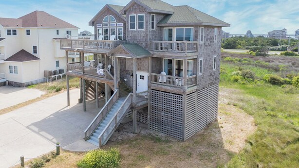 A multi-story beachfront house with a balcony, a staircase, and a view of the beach. - Semi-Oceanfront Home w/ Hot Tub, Smart TVs, Community Tennis/Pickleball Courts (Rodanthe)