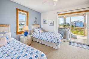Une chambre avec deux lits, une fenêtre, un ventilateur de plafond et un balcon donnant sur des immeubles.