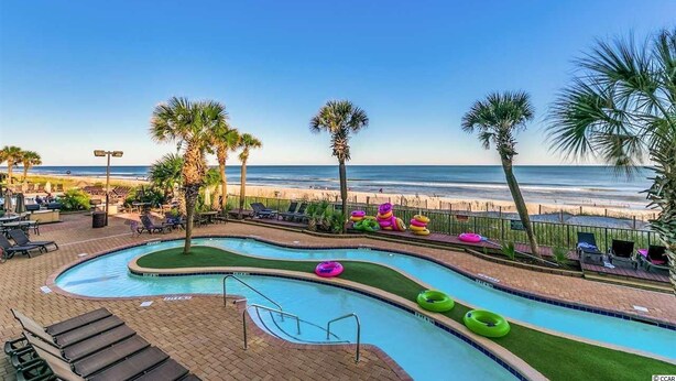 Un espace piscine avec vue sur la plage, des chaises longues et des palmiers.
