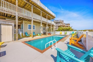 Uma área de piscina com deck de madeira, cadeiras e um edifício com varandas.