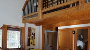 A spacious living room with a high ceiling, wooden flooring, a black leather sofa, a yellow throw blanket, and a small table with a candle. - Beautiful eco-building in the heart of the Rocky mountains. All modern amenities (golden)