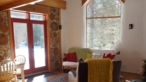 A cozy living room with a wooden ceiling, a large window, a sofa, and a dining area with chairs. - Beautiful eco-building in the heart of the Rocky mountains. All modern amenities (golden)