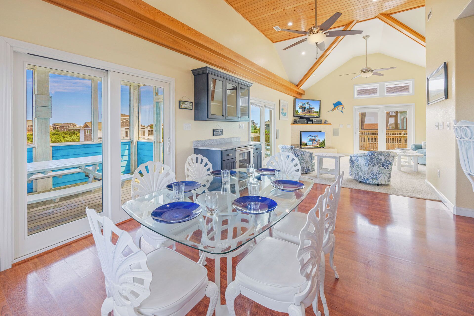 Uma sala de estar ampla com uma mesa de jantar de vidro, cadeiras brancas e vista para o oceano.