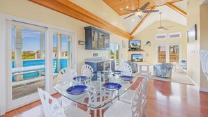 A spacious living area with a glass dining table, white chairs, and a view of the ocean. - Oceanview Dog Friendly Home with Private Pool, Hot Tub, Elevator, Game Room (Avon)