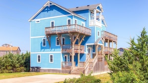 A large, two-story house with a prominent balcony and a wooden staircase leading to the upper floor. - Oceanview Dog Friendly Home with Private Pool, Hot Tub, Elevator, Game Room (Avon)