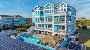 A multi-story building with balconies, a swimming pool, and solar panels. - Premier Oceanview Dog Friendly w/ Pool, Hot Tub, Elevator, EV Charger, Much More (Rodanthe)