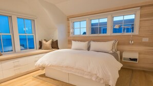A bedroom with a large bed, built-in storage, a window seat, and a view of the sea. - Spectacular Beachfront West End Home  (Provincetown)