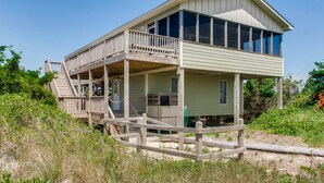 A coastal wooden structure with a balcony, a covered area, and a staircase leading to the upper level.