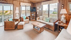 A cozy, wood-paneled living room with a large window, a bookshelf, and a flat-screen TV.
