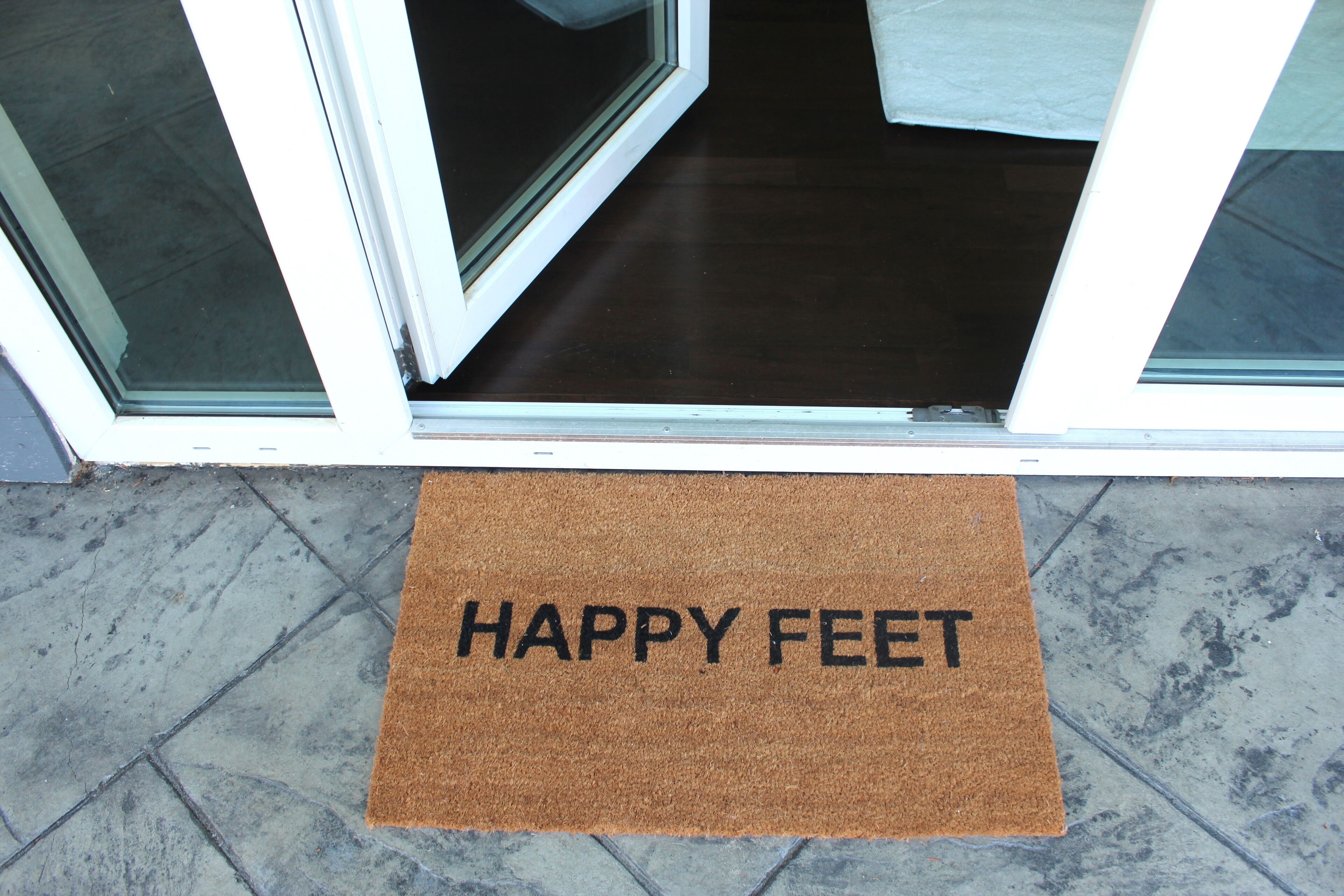 Eine braune Fußmatte mit dem Aufdruck 'HAPPY FEET' vor einem Hauseingang.