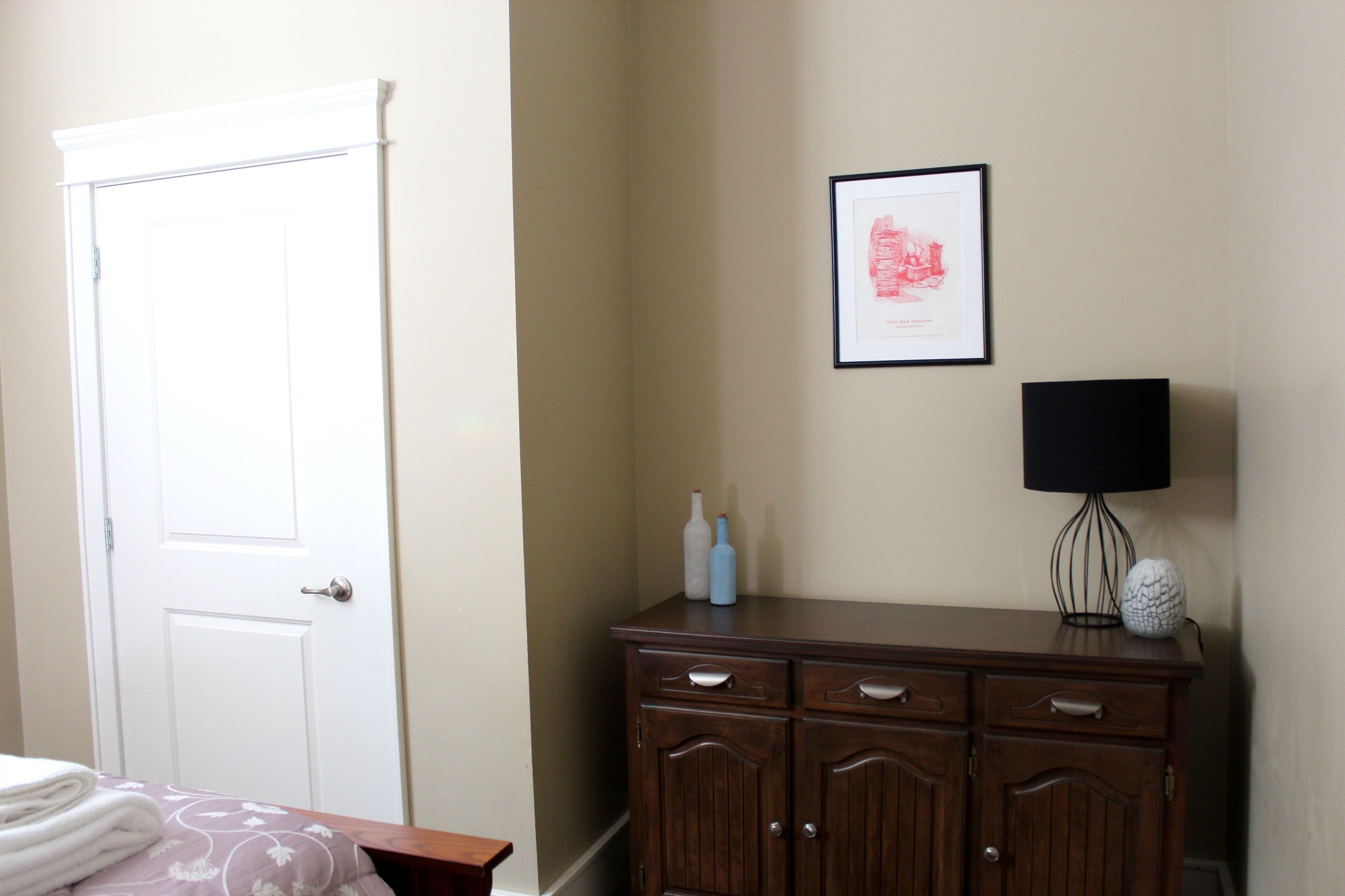 A bedroom with a bed, a dresser, a framed picture, and a lamp.