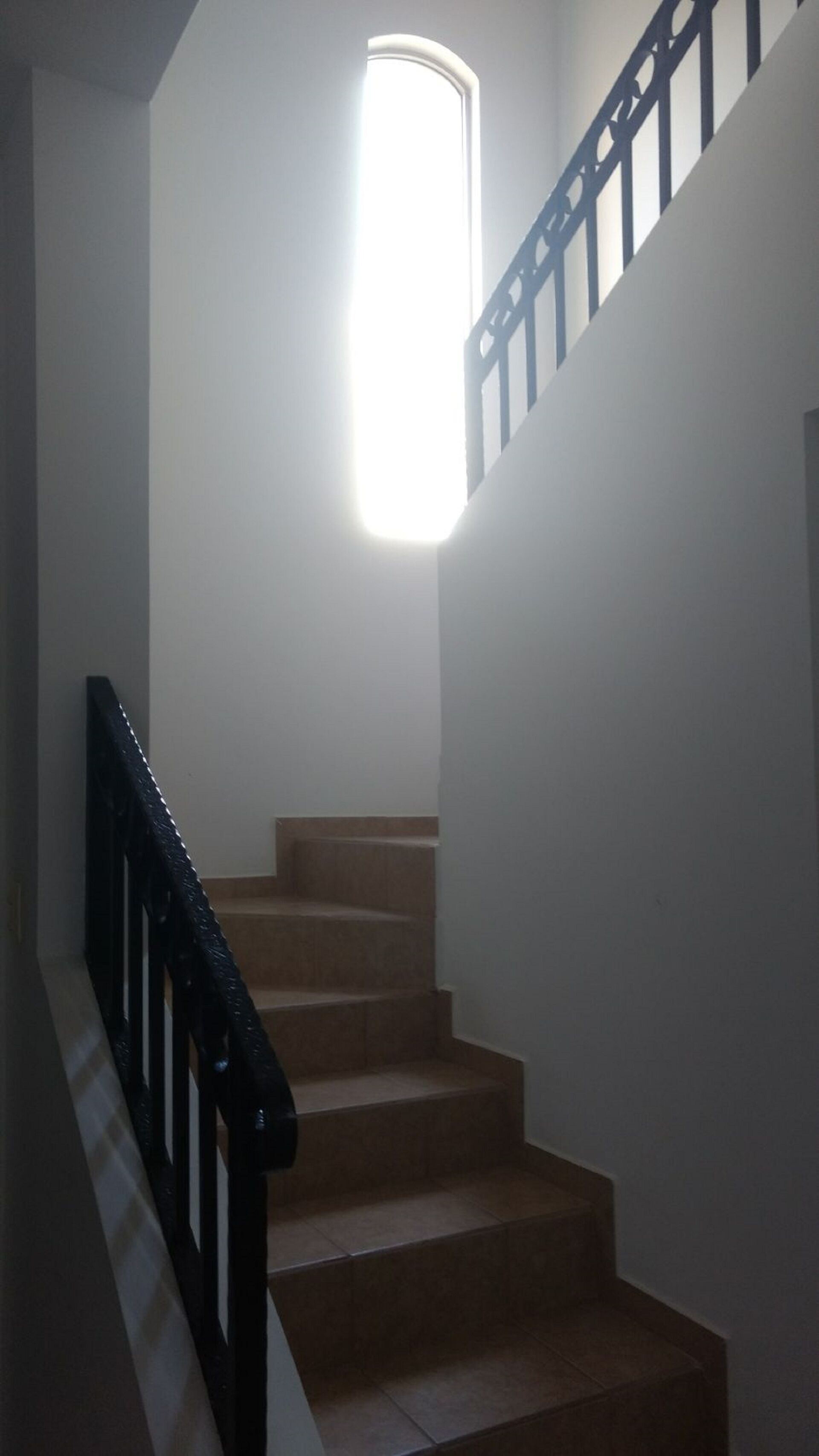 A staircase with a black handrail and a light fixture above it.