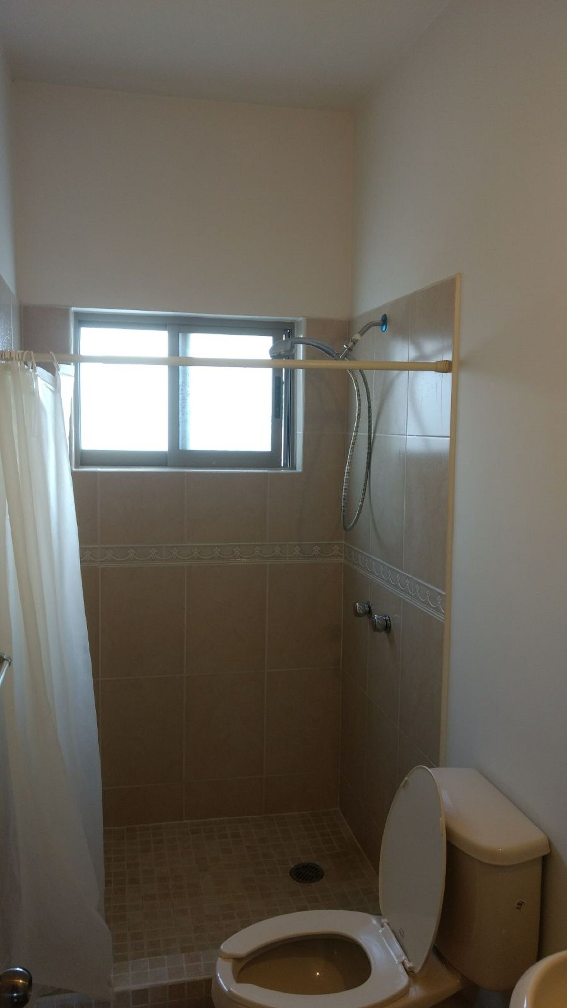 Un petit espace douche fermé, doté d’une fenêtre, de toilettes et d’un pommeau de douche.