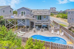 A beachfront property with a swimming pool, deck chairs, and a wooden deck.
