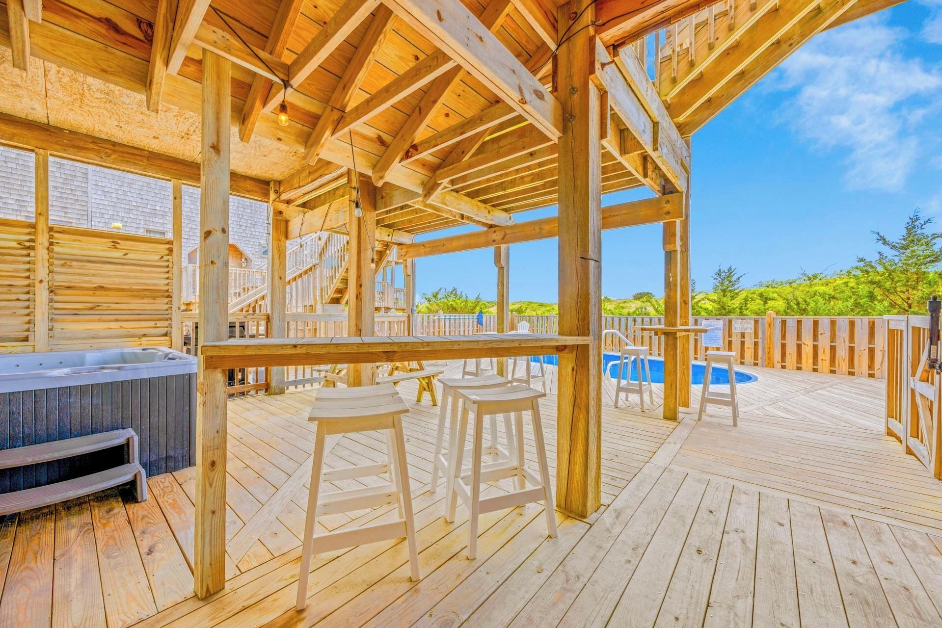 Une terrasse en bois avec un jacuzzi, deux chaises blanches et une piscine.