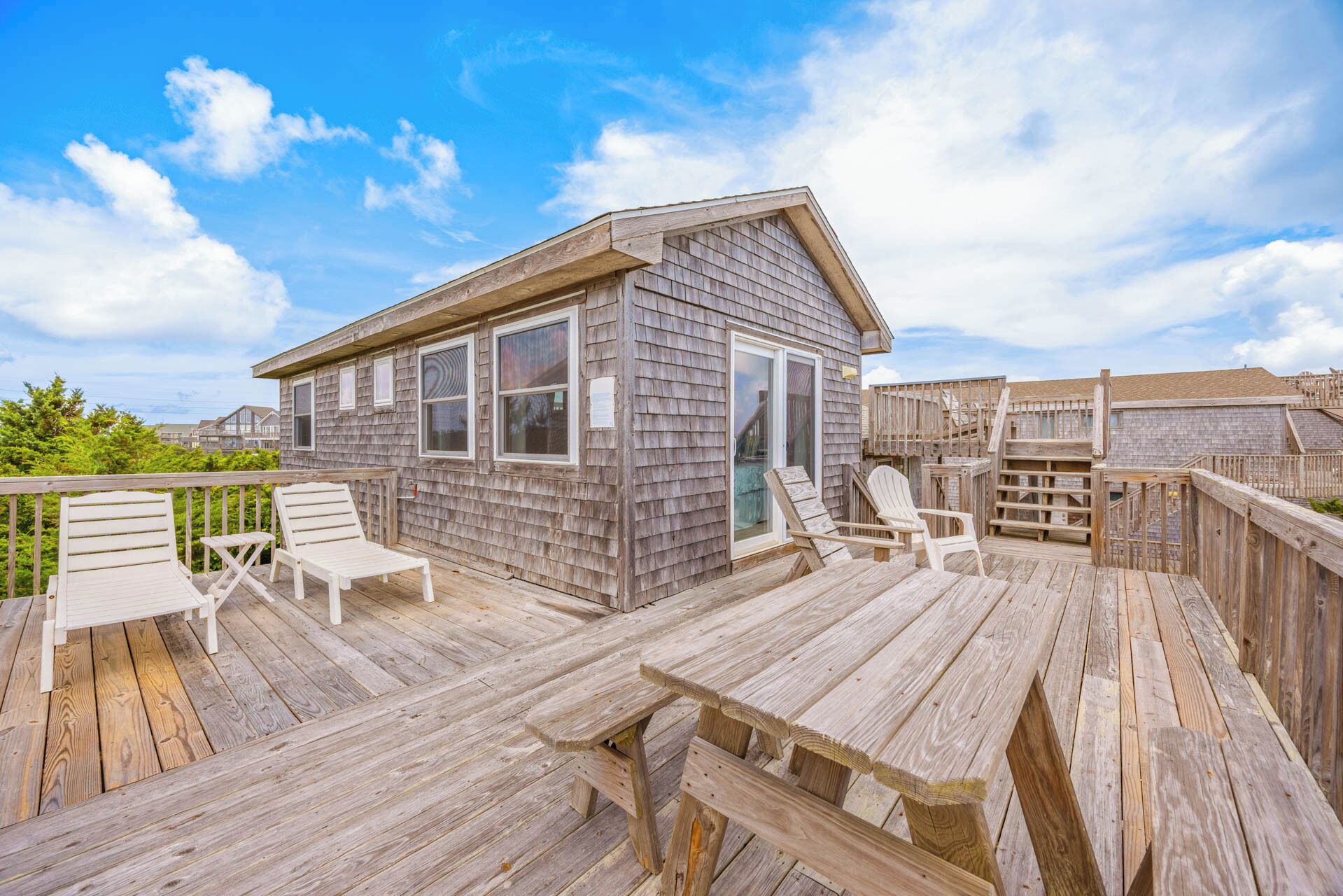 A wooden deck with lounge chairs, a small wooden building, and a wooden staircase.