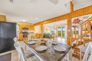 A spacious kitchen with modern appliances, a dining area with a wooden table set for four, and a staircase leading to a loft bedroom.