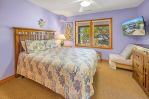 A bedroom with a bed, a nightstand, a lamp, a dresser, a chair, a window, and a ceiling fan.