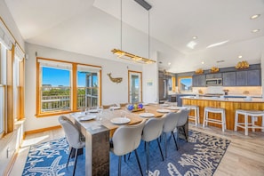 A modern kitchen with a central island, bar stools, and a dining area with a large window.