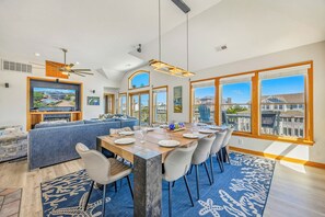 A spacious dining area with a long table, multiple chairs, and a view of the neighborhood through large windows.