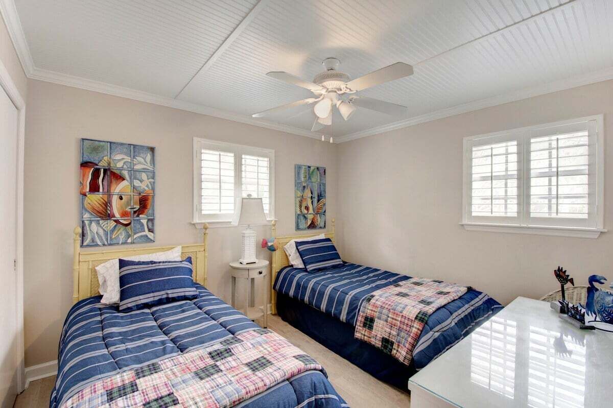 A bedroom with two beds, a ceiling fan, and artwork on the walls.