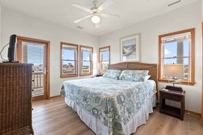 A bedroom with a large bed, a ceiling fan, and a view of the outside through the windows.
