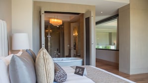 A hotel room with a bed, pillows, a bedside lamp, a sign, and a view of a bathroom with a bathtub and shower. - Grand Luxxe Riviera Maya 3 Bedroom Residence (SPRING BREAK 2020 - 3/14-21) (Riviera Maya)