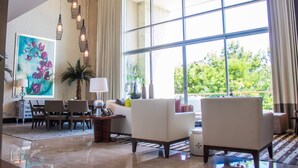 A spacious living room with a large window, a dining area, and a painting on the wall. - Grand Luxxe Riviera Maya 3 Bedroom Residence (SPRING BREAK 2020 - 3/14-21) (Riviera Maya)