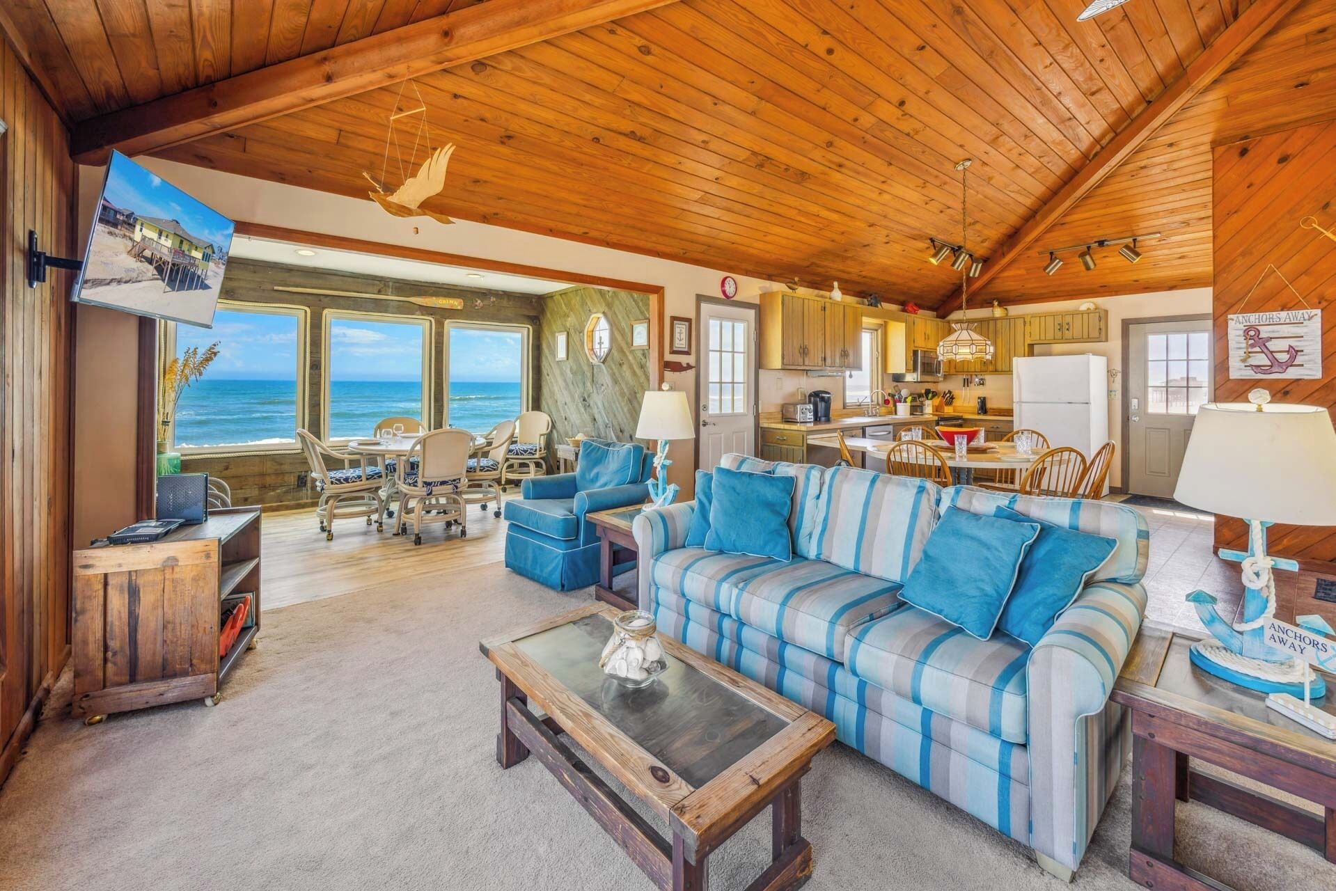 A cozy cabin interior with a large window overlooking the ocean, a dining area, and a kitchen.
