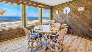 A dining area with a view of the beach, wooden walls, and wicker chairs. - Cozy Oceanfront Cottage w/ Books, Games, TVs, Stunning Views. Right on the Beach (Rodanthe)
