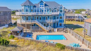 A multi-story house with a large backyard featuring a swimming pool, deck chairs, and a wooden fence.