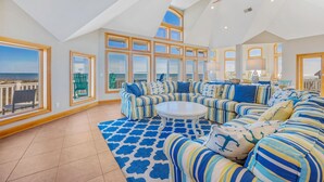A spacious living room with a large sectional sofa, a round coffee table, and a view of the ocean through large windows.