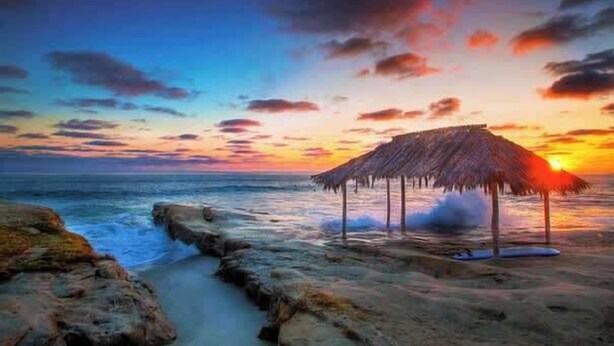 A beach scene with a thatched-roof structure, rocky shoreline, and ocean waves. - Driftwood your perfect beach getaway! (La Jolla)