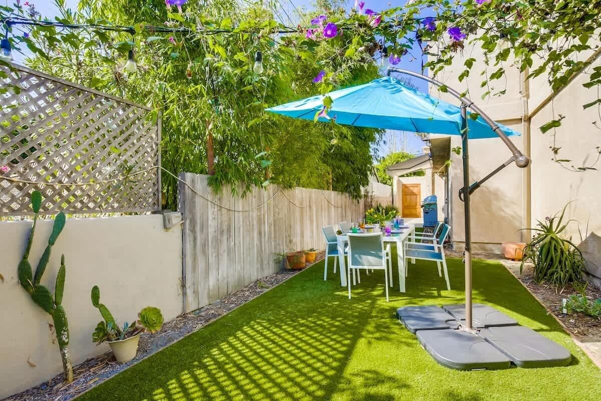 Un patio con una mesa y sillas, un paraguas azul y plantas en macetas.