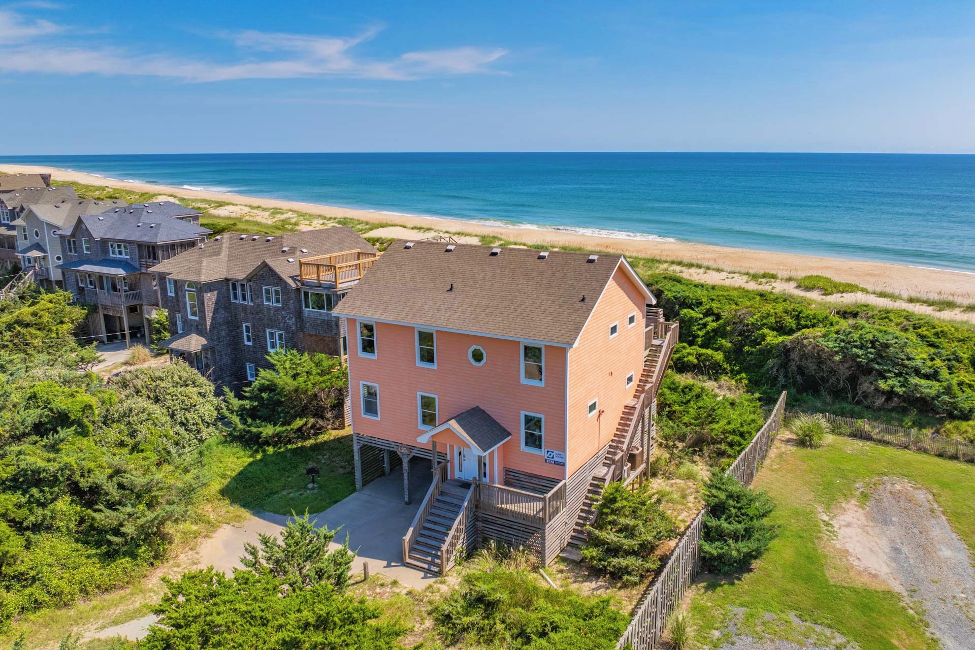 A coastal property with a prominent pink building, a beach view, and a forested area.