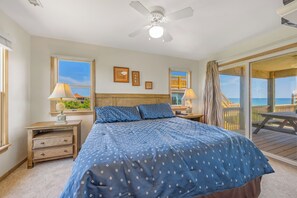 A bedroom with a bed, two bedside tables, a ceiling fan, and a view of the ocean through a sliding glass door. - Oceanfront Home in Avon with Hot Tub, Community Pool and Tennis/Pickleball (Avon)
