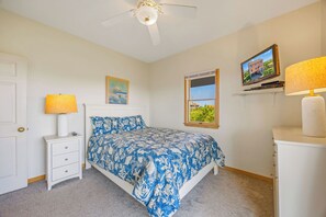 A bedroom with a bed, a nightstand, a lamp, a ceiling fan, a window, and a TV on a shelf.