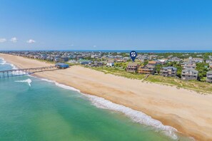 A coastal residential area with a pier extending into the ocean, houses with various architectural styles, and a clear sky. - Oceanfront Home in Avon with Hot Tub, Community Pool and Tennis/Pickleball (Avon)