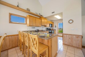 A kitchen with wooden cabinets, a granite countertop, and a dining area with chairs. - Oceanfront Home in Avon with Hot Tub, Community Pool and Tennis/Pickleball (Avon)
