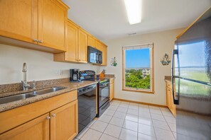 A kitchen with wooden cabinets, stainless steel appliances, a window with a view, and a tiled floor. - Oceanfront Home in Avon with Hot Tub, Community Pool and Tennis/Pickleball (Avon)