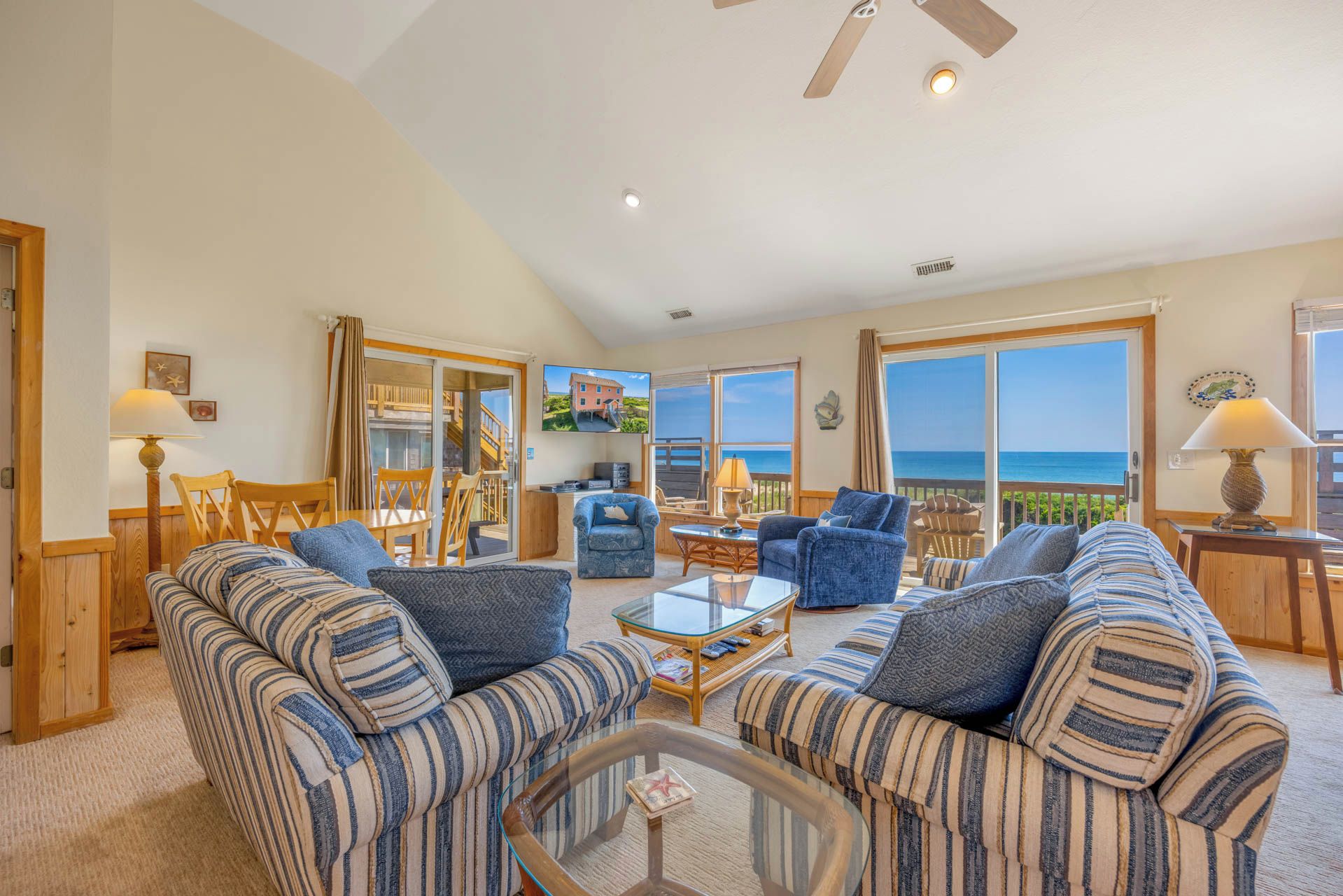 A spacious living room with striped sofas, a glass coffee table, and a view of the ocean through large windows.