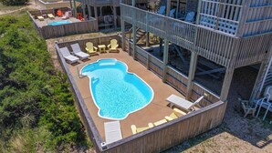 Una terraza de madera con piscina, sillas de descanso y una zona de estar cubierta.