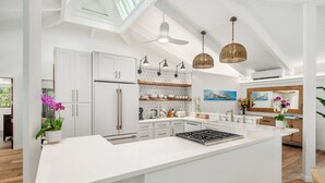A modern kitchen with white cabinetry, a central island, pendant lighting, and a ceiling fan.